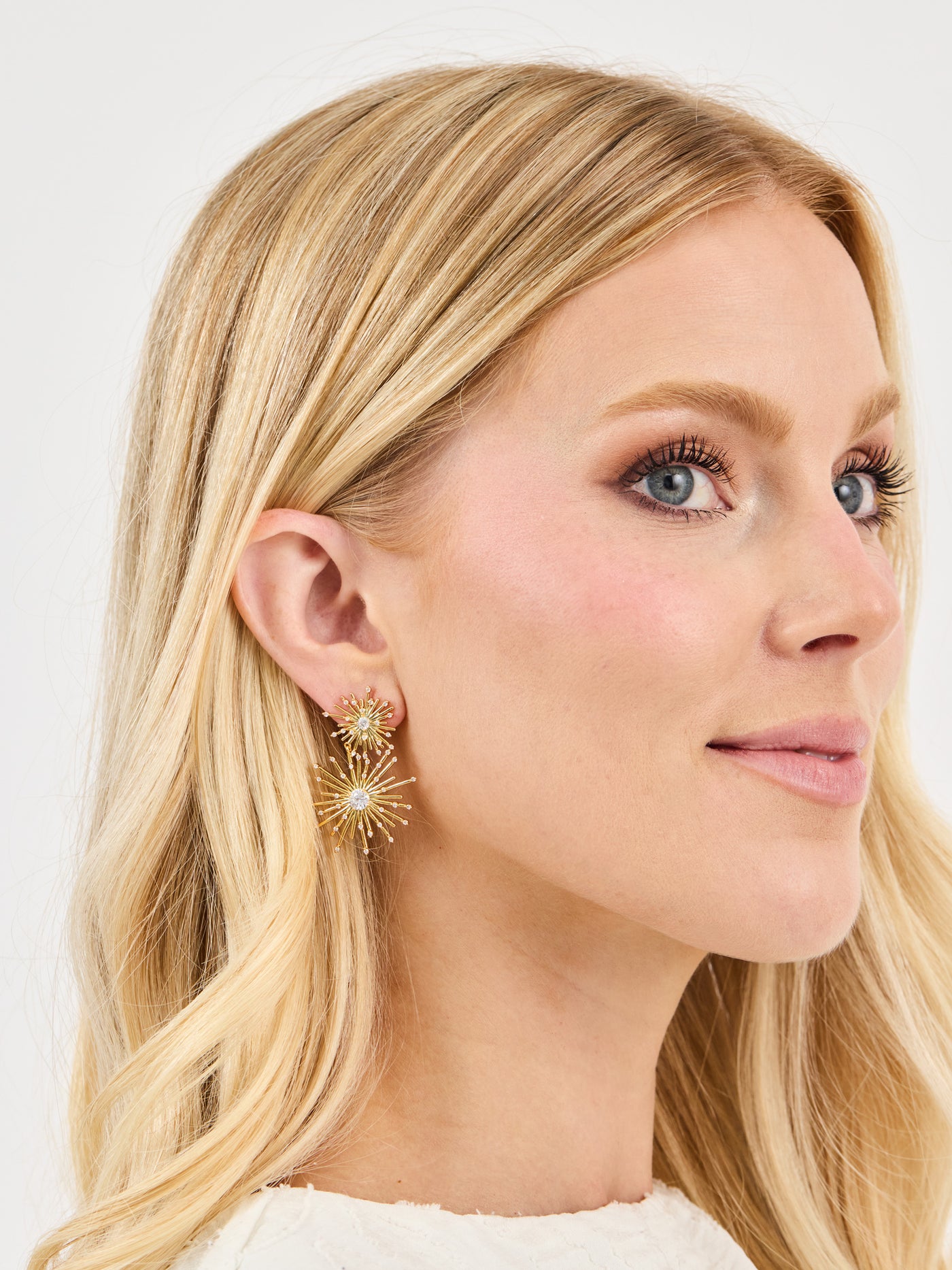 Close-up of a woman wearing gold earrings with a plain background