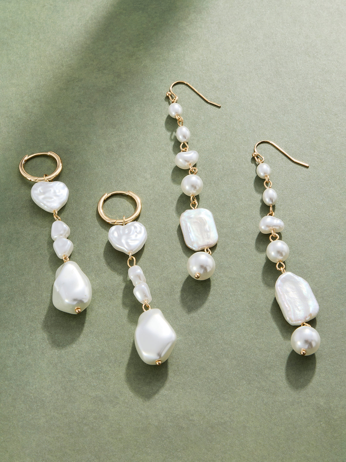 Three pairs of gold-tone dangle earrings with irregular white pearls and small pearl beads, arranged on a muted sage green background.
